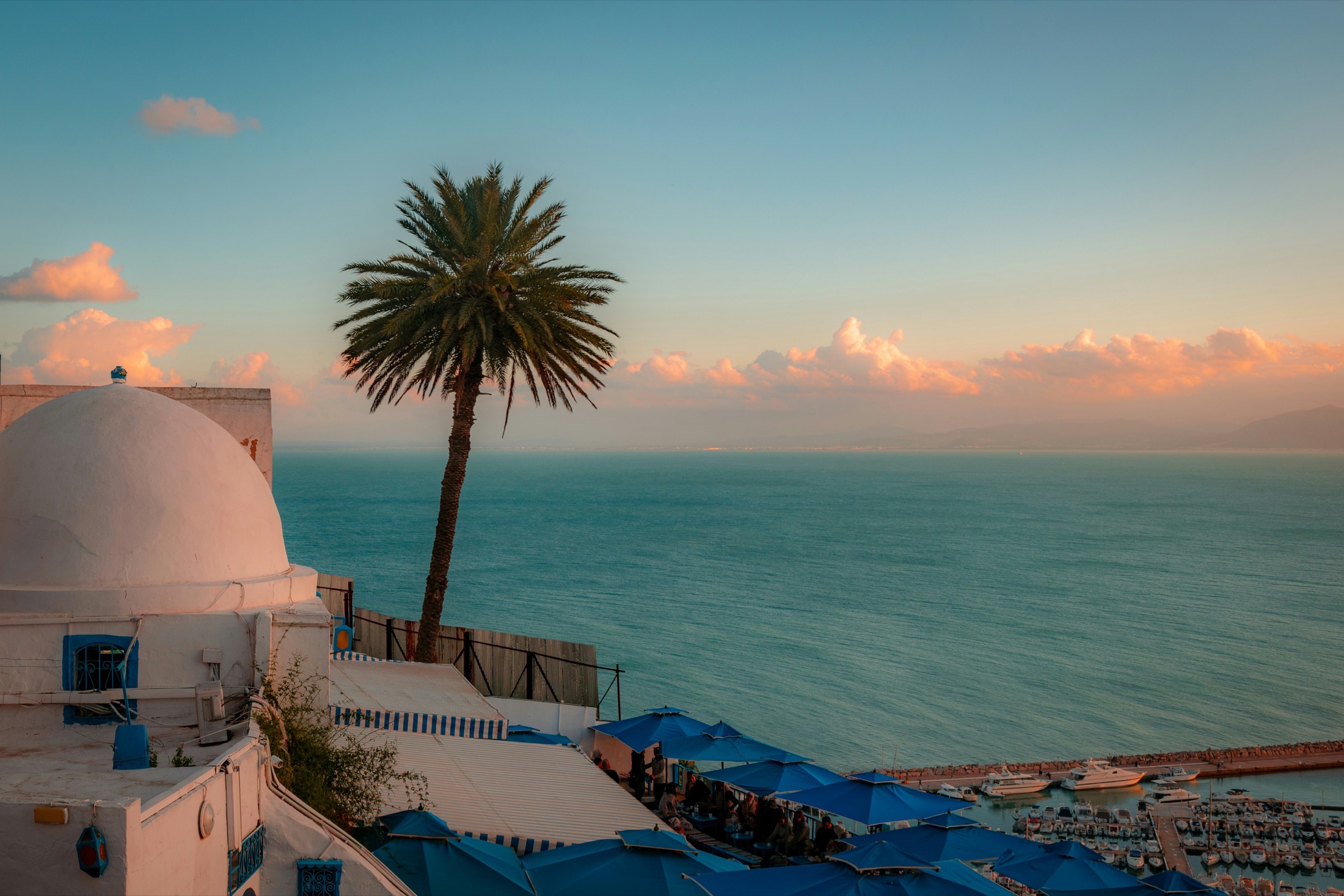 A whitewashed dome overlooking a Tunisian fishing harbor at sunset